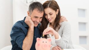 A couple putting cash in a piggy bank, representing cash savings for a UK spouse visa application in 2026.