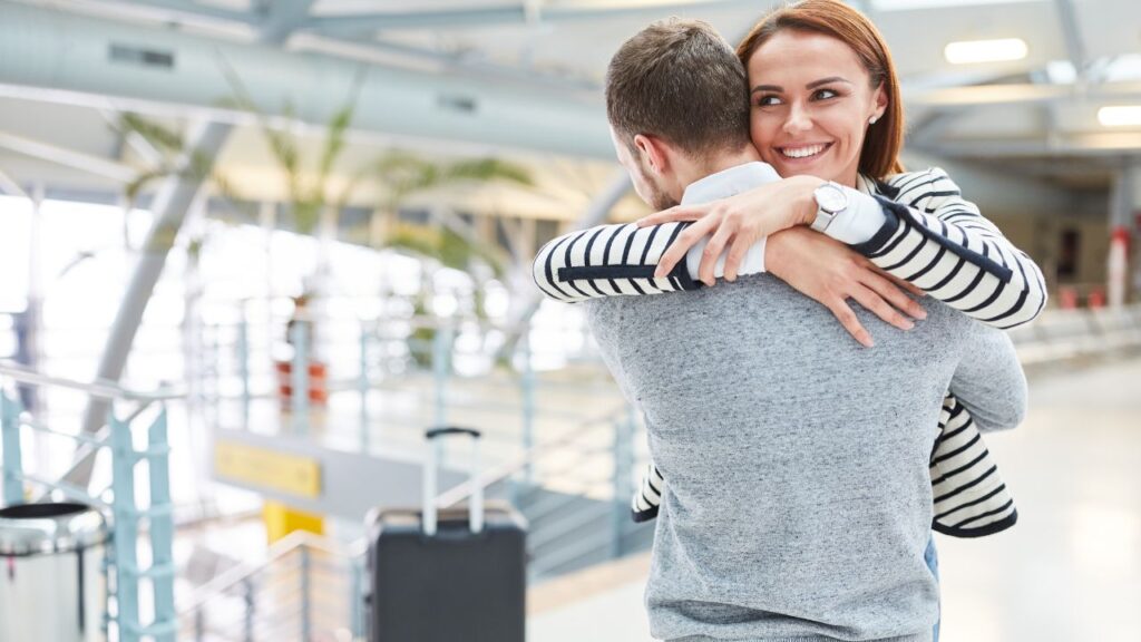 A British man welcoming his wife at a London airport arrivals hall after a UK partner visa was granted.