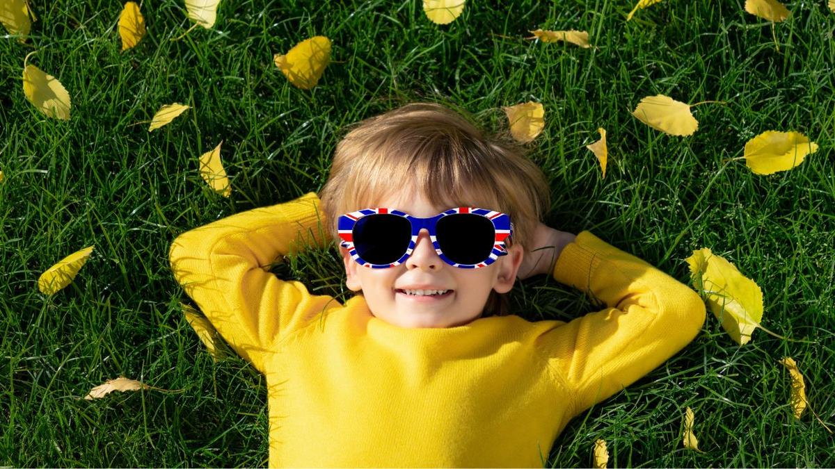 British Citizenship for Child & UK Spouse Visa Success Smiling child in Union flag sunglasses lying on autumn leaves, illustrating British citizenship by registration for a child born abroad