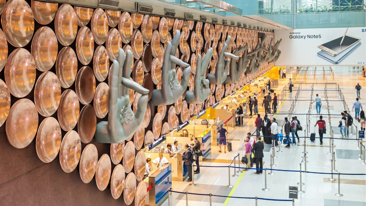 Indian e-Arrival Landing Card Delhi airport arrivals hall with its wall of copper hand mudra sculptures above passengers queueing, illustrating India's new e-Arrival card
