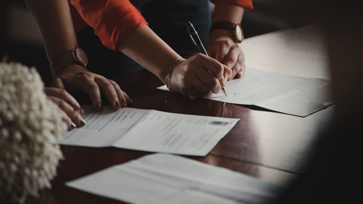 Indian POA Format Two people signing documents at a dark wooden table, illustrating the format and wording of an Indian Power of Attorney