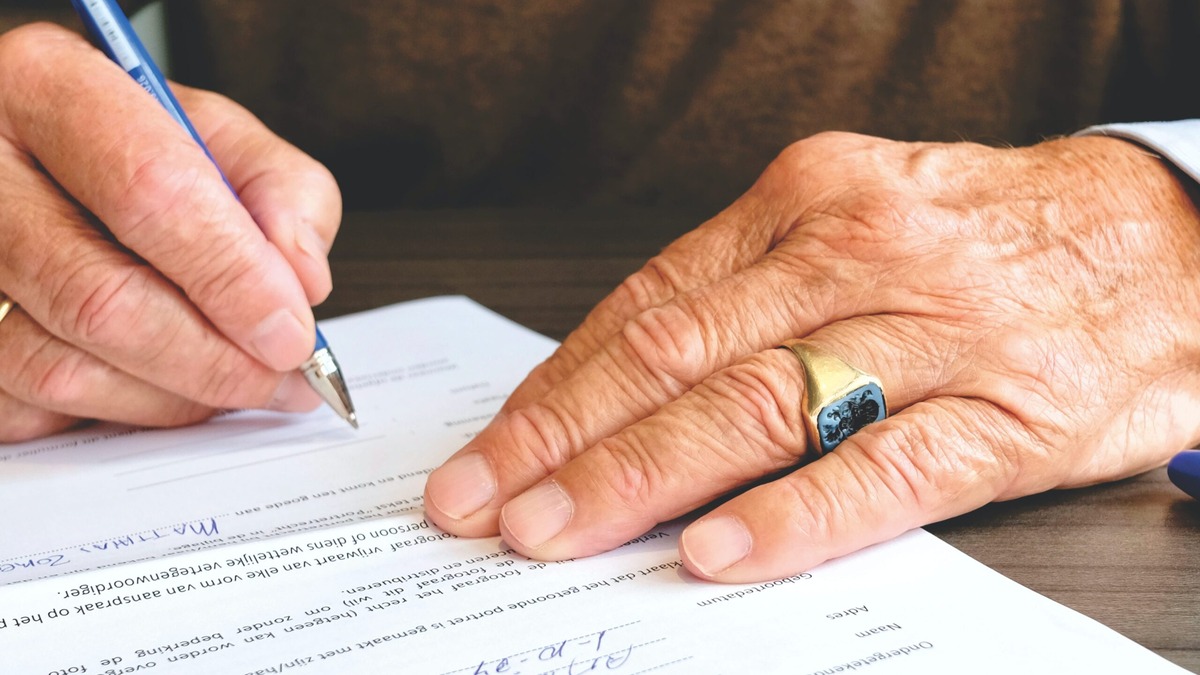 Sell Indian Property Indian POA Older man's hand signing a document with a ballpoint pen, illustrating the role of an Indian Power of Attorney in property mutation