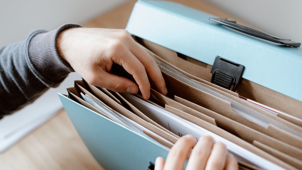 OCI Card Application Documents Hands sorting papers in a blue expanding file, gathering the documents needed for an OCI card application