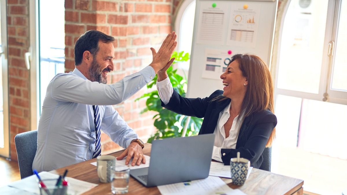 UK Ancestry Visa Employment Two colleagues sharing a high five at an office desk, illustrating the employment requirement for the UK Ancestry visa