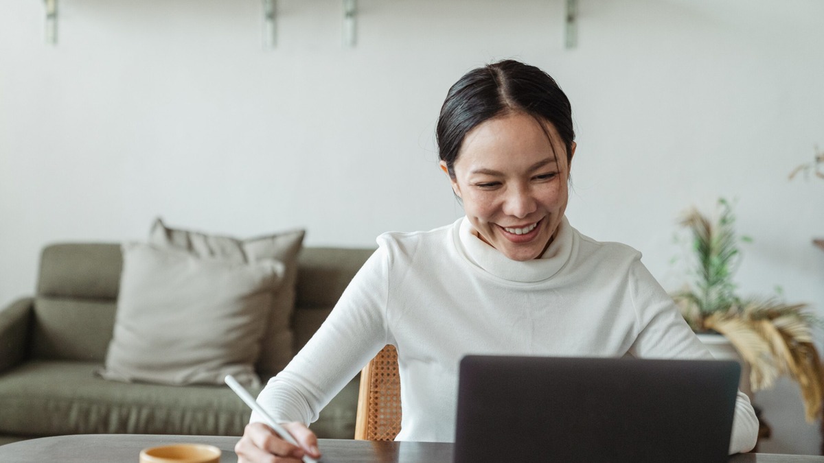 UK-Residence-Documents Woman smiling as she writes notes at her laptop, gathering documents to prove continuous residence in the UK